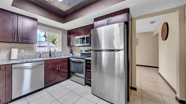 kitchen featuring stainless steel appliances, a sink, light tile patterned floors, light stone counters, and baseboards