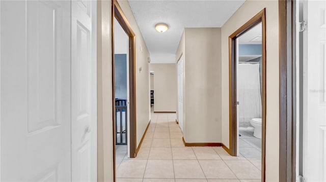 corridor with light tile patterned floors, baseboards, and a textured ceiling