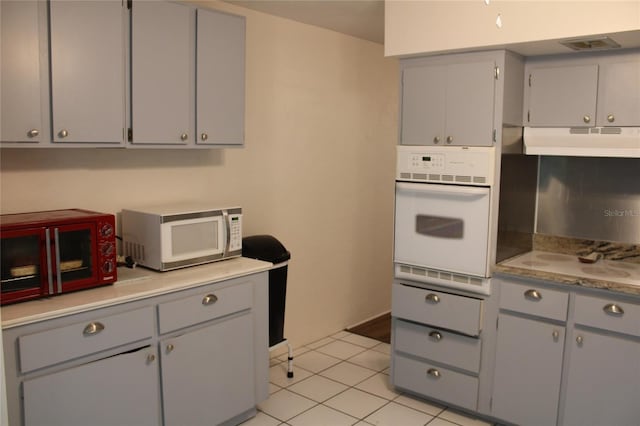 2020 World Parkway Blvd Unit 12, Clearwater, FL 33763 - kitchen featuring white appliances, gray cabinetry, under cabinet range hood, light tile patterned flooring, and light countertops
