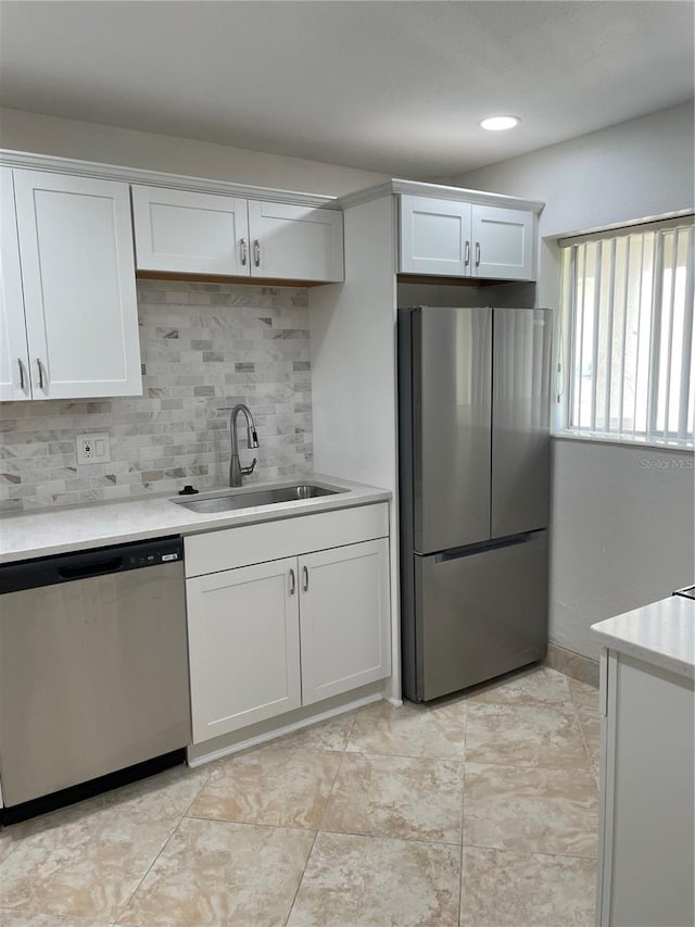 kitchen featuring appliances with stainless steel finishes, a sink, tasteful backsplash, light countertops, and white cabinets