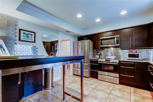3406 Hollyhock Way, Tampa, FL 33618 - kitchen featuring appliances with stainless steel finishes, tasteful backsplash, dark brown cabinetry, light tile patterned flooring, and light stone counters