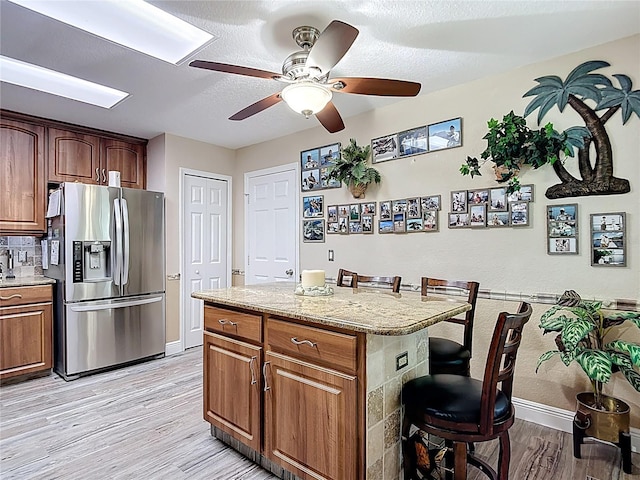 1628 Lullwater Ln, Lutz, FL 33549 - kitchen with stainless steel refrigerator with ice dispenser, a breakfast bar area, baseboards, light wood-type flooring, and a ceiling fan