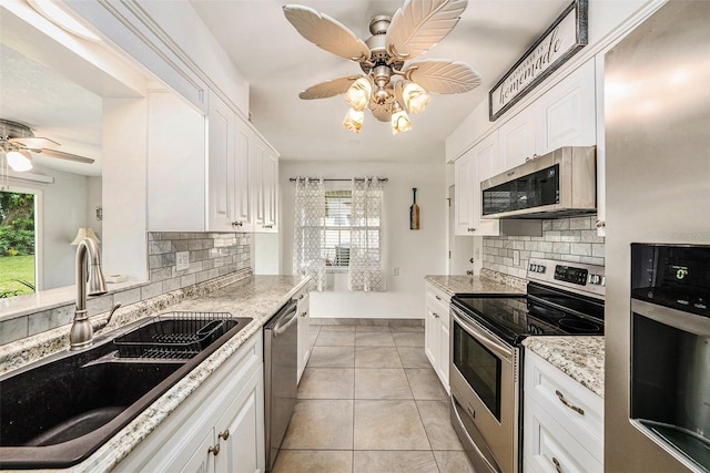 kitchen featuring stainless steel appliances, a sink, a ceiling fan, white cabinetry, and decorative backsplash