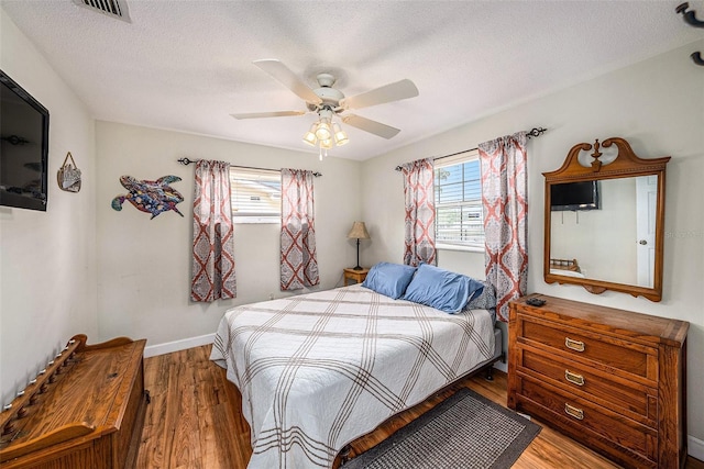 bedroom featuring multiple windows, wood finished floors, a ceiling fan, a textured ceiling, and baseboards