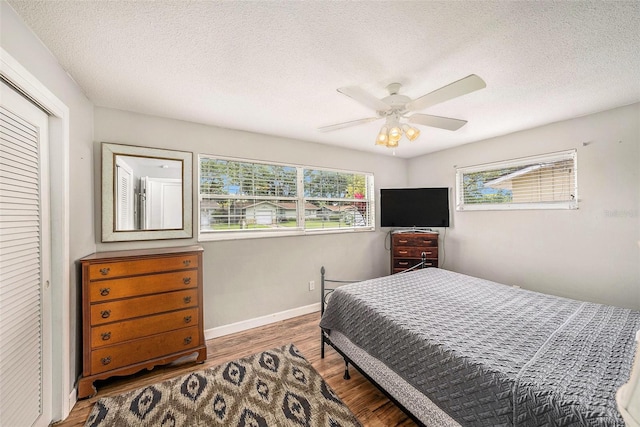 bedroom featuring multiple windows, wood finished floors, a textured ceiling, a closet, and ceiling fan
