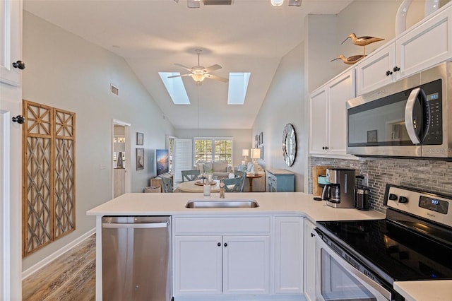 kitchen with appliances with stainless steel finishes, a peninsula, a skylight, a sink, and light wood-style flooring