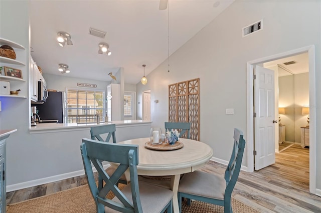 dining area with light wood-type flooring, baseboards, and high vaulted ceiling