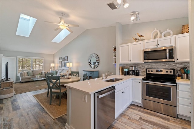 kitchen with stainless steel appliances, a skylight, a sink, light wood-style flooring, and high vaulted ceiling