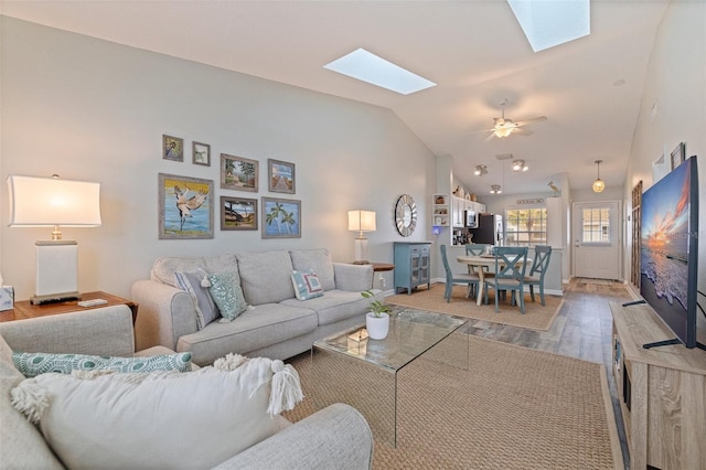 living area with a skylight, wood finished floors, lofted ceiling, baseboards, and ceiling fan