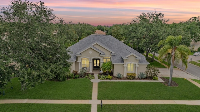 view of front of property with french doors, a yard, roof with shingles, stucco siding, and concrete driveway