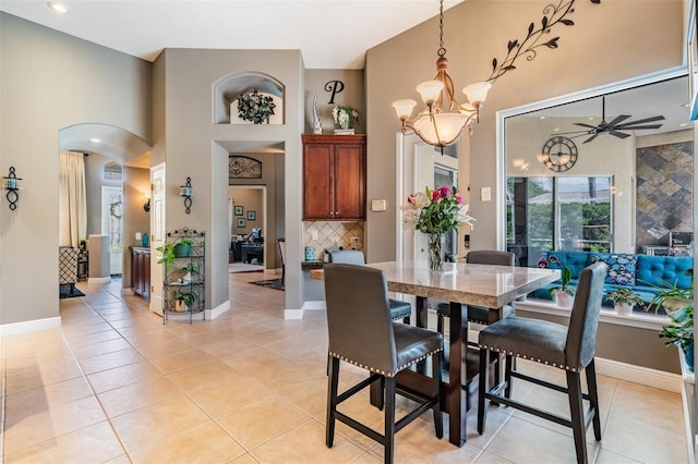 dining space featuring a chandelier, arched walkways, light tile patterned floors, a ceiling fan, and baseboards