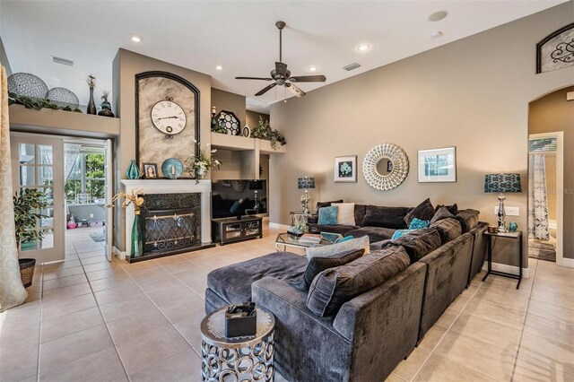 living room featuring a high ceiling, a ceiling fan, tile patterned flooring, arched walkways, and a high end fireplace
