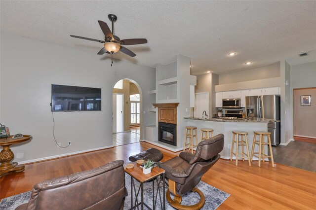 living room featuring arched walkways, wood finished floors, a textured ceiling, ceiling fan, and baseboards
