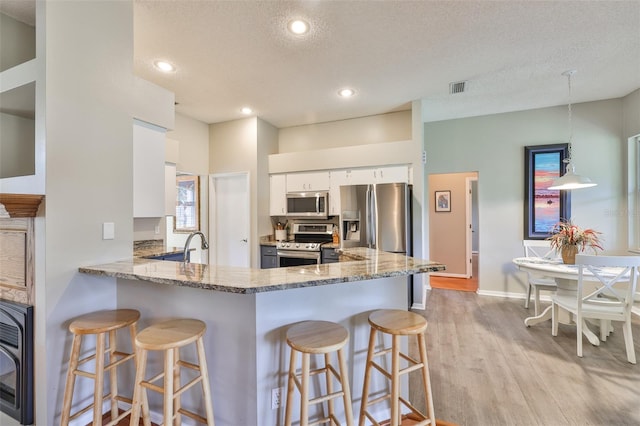 kitchen with stainless steel appliances, light wood-style floors, white cabinetry, a peninsula, and light stone counters