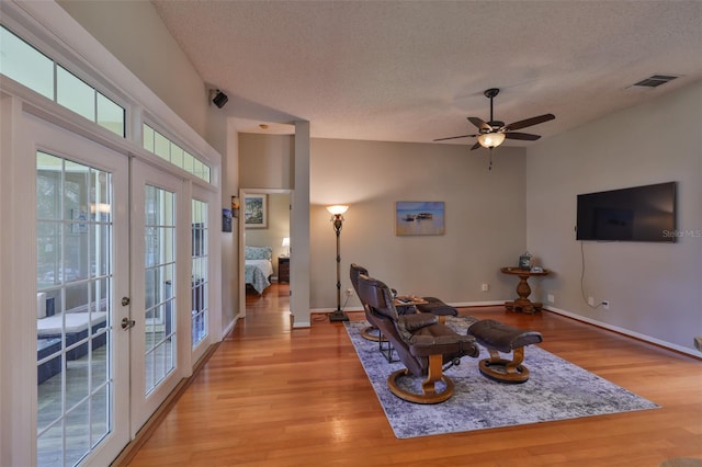 living area with french doors, a textured ceiling, light wood-style floors, a ceiling fan, and baseboards