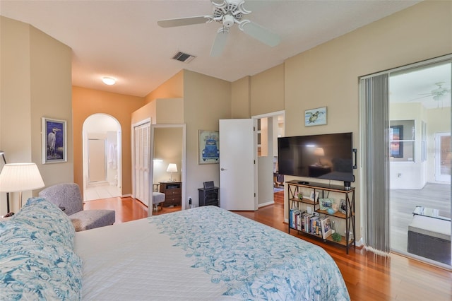 bedroom featuring arched walkways, wood finished floors, ensuite bathroom, vaulted ceiling, and a ceiling fan