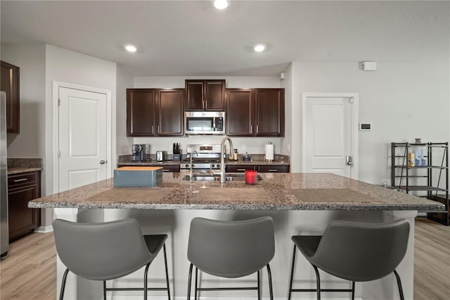 9640 Lemon Drop Loop, Ruskin, FL 33573 - kitchen with stainless steel appliances, a breakfast bar, a sink, light wood-style floors, and dark brown cabinets