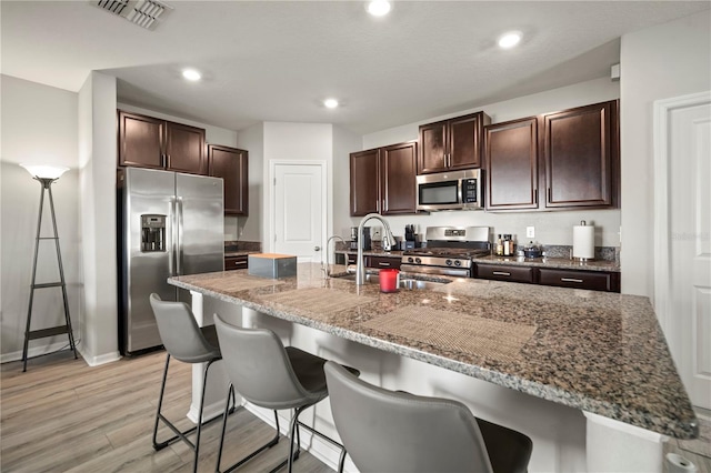 9640 Lemon Drop Loop, Ruskin, FL 33573 - kitchen with appliances with stainless steel finishes, a sink, a breakfast bar, dark brown cabinets, and dark stone counters