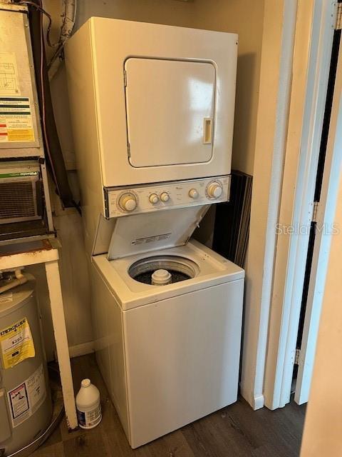 laundry room with stacked washer / dryer, electric water heater, and dark wood-style floors