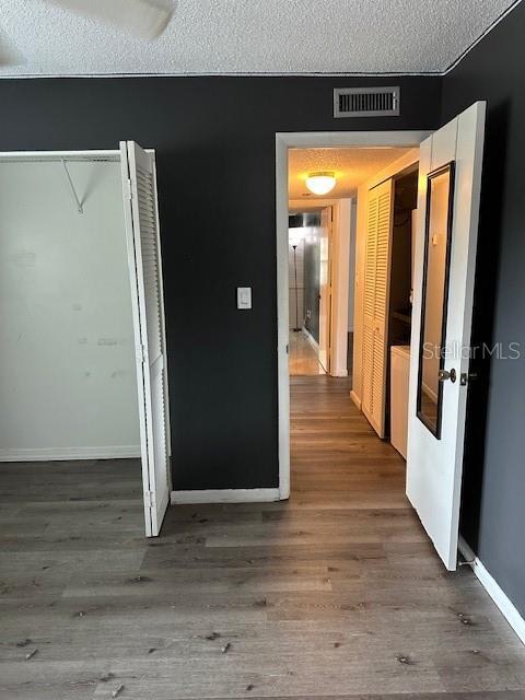 hallway featuring a textured ceiling, wood finished floors, and baseboards