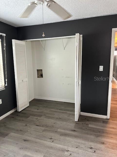 unfurnished bedroom featuring a textured ceiling, wood finished floors, a closet, baseboards, and ceiling fan