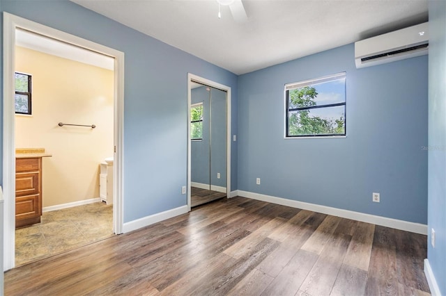 1225 15th St, Palm Harbor, FL 34683 - unfurnished bedroom with an AC wall unit, wood finished floors, connected bathroom, and baseboards