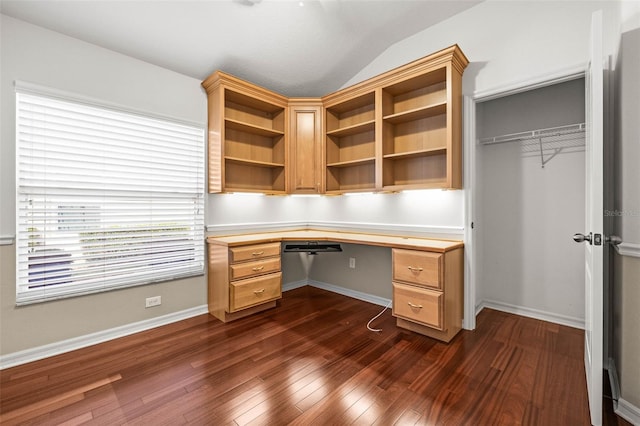 unfurnished office featuring vaulted ceiling, built in desk, dark wood-style floors, and baseboards