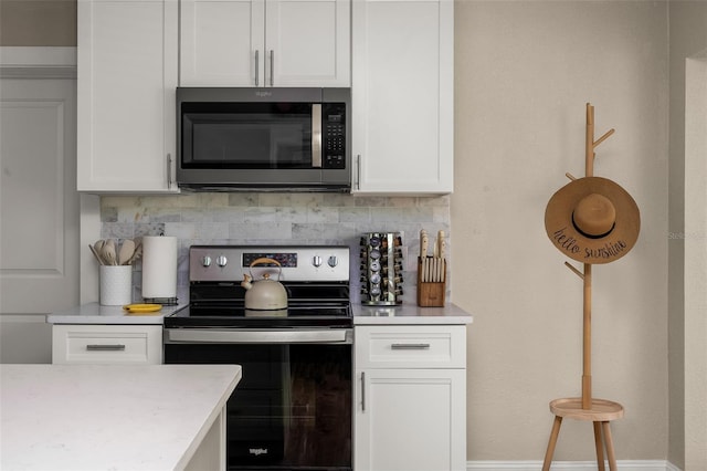 616 11th St NW, Largo, FL 33770 - kitchen featuring stainless steel microwave, electric range oven, decorative backsplash, white cabinetry, and baseboards