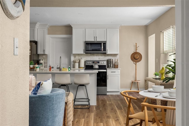 616 11th St NW, Largo, FL 33770 - kitchen featuring appliances with stainless steel finishes, light wood-type flooring, white cabinets, and tasteful backsplash