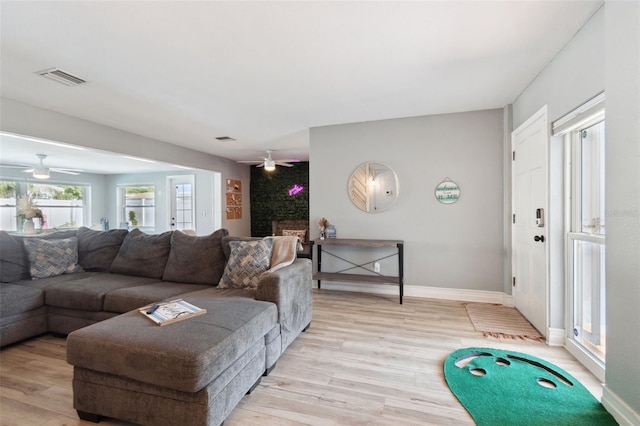 living area with a ceiling fan, light wood finished floors, baseboards, and a large fireplace