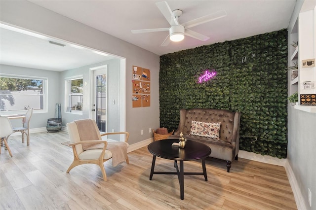 living area featuring an accent wall, a ceiling fan, light wood-style floors, and baseboards