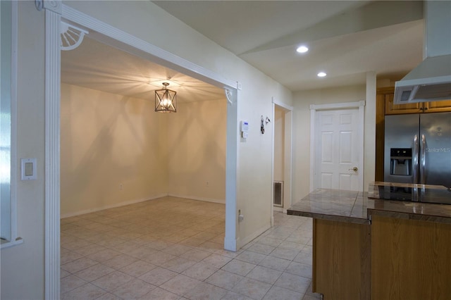 8209 Chaucer Dr, Weeki Wachee, FL 34607 - kitchen featuring stainless steel fridge with ice dispenser, wall chimney exhaust hood, light tile patterned flooring, recessed lighting, and brown cabinetry