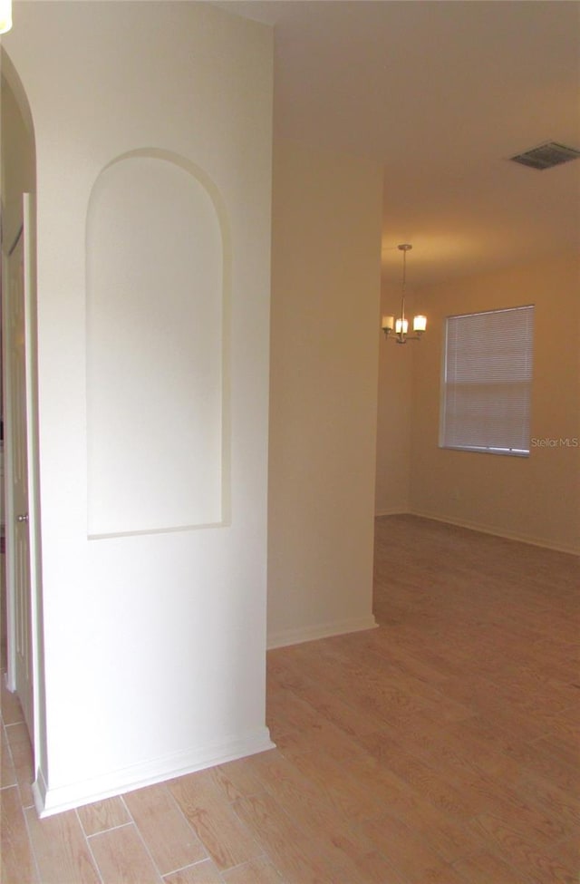 unfurnished room with light wood-style flooring, a chandelier, arched walkways, and baseboards