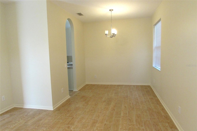spare room featuring arched walkways, light wood-style floors, and healthy amount of natural light