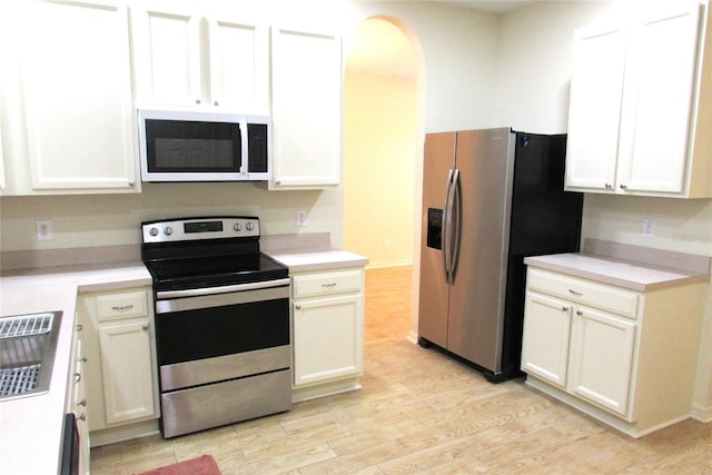 kitchen featuring stainless steel appliances, light wood-style floors, light countertops, arched walkways, and white cabinetry