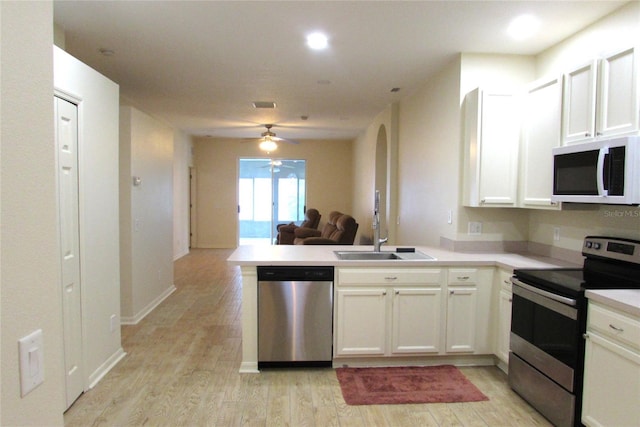 kitchen with stainless steel appliances, a peninsula, a sink, light wood-style floors, and open floor plan