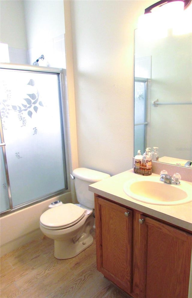 full bathroom with wood finished floors, shower / bath combination with glass door, vanity, and toilet