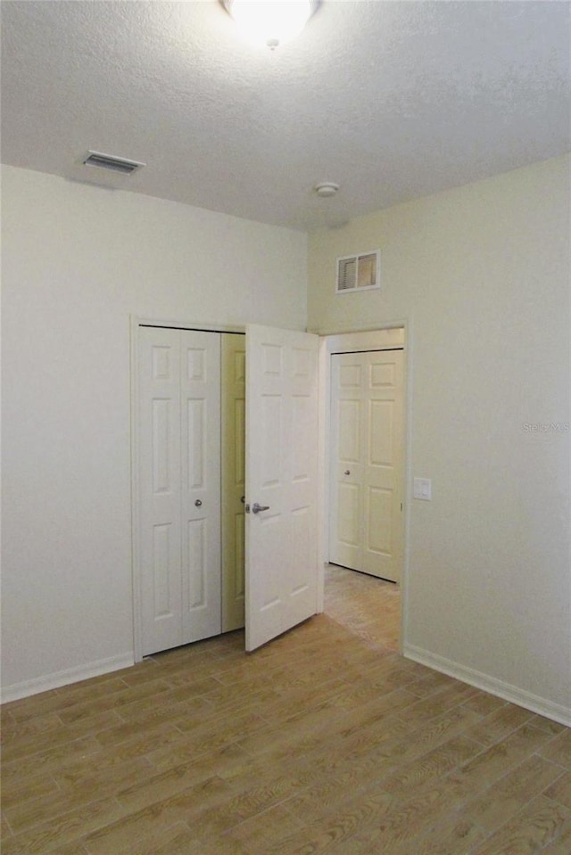 empty room with light wood-style floors, baseboards, a textured ceiling, and a smoke detector
