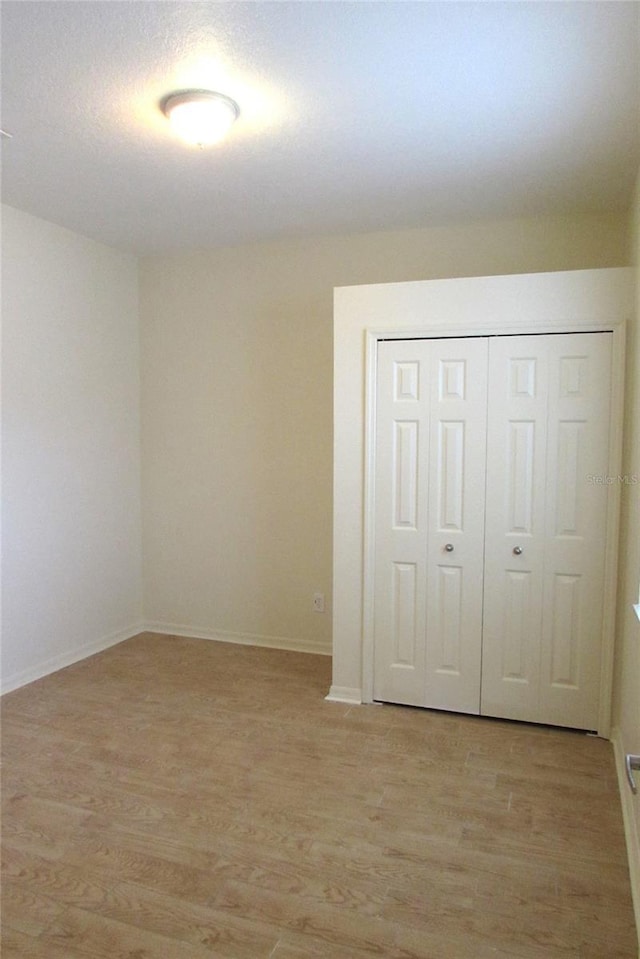unfurnished bedroom with light wood-style flooring, a closet, and baseboards