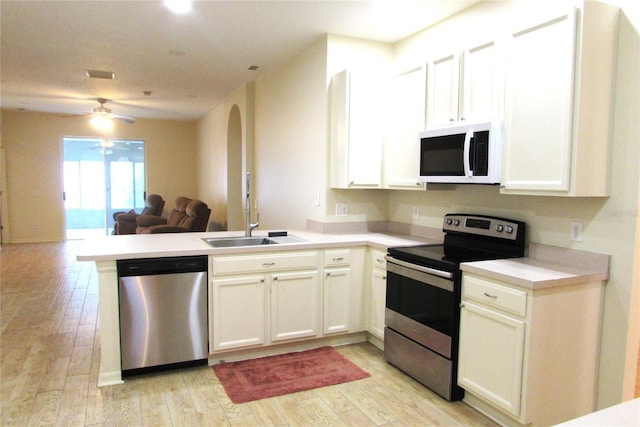 kitchen with stainless steel appliances, a peninsula, open floor plan, a ceiling fan, and light wood finished floors