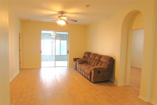 living room featuring a ceiling fan, light wood-type flooring, arched walkways, and baseboards