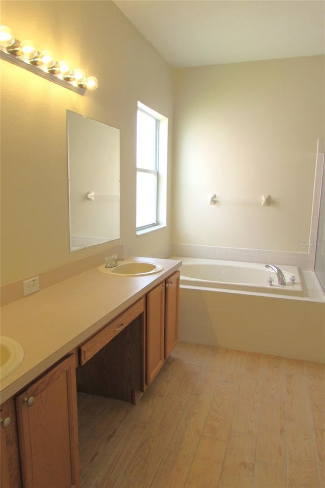 full bath with wood finished floors, a garden tub, and vanity