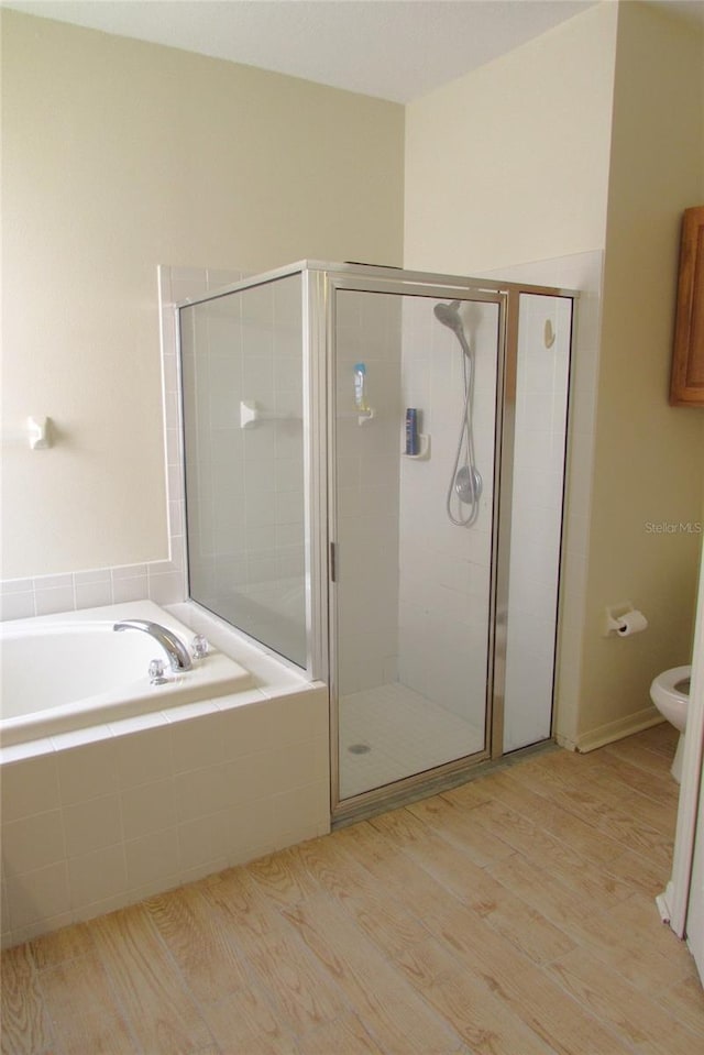 bathroom featuring a stall shower, a bath, wood finished floors, and toilet