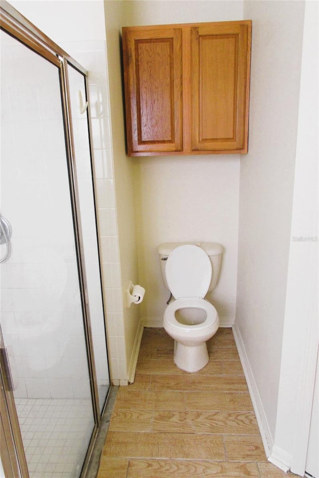 bathroom with wood finished floors, a stall shower, toilet, and baseboards