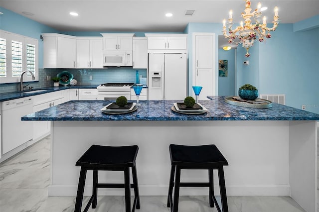 kitchen featuring white appliances, a sink, a center island, white cabinetry, and decorative backsplash