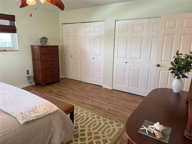 bedroom featuring multiple closets, wood finished floors, baseboards, and a ceiling fan
