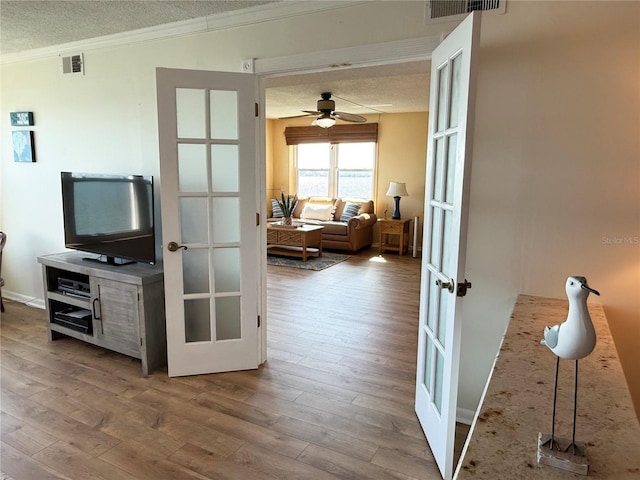 interior space with crown molding, wood finished floors, french doors, a textured ceiling, and a ceiling fan