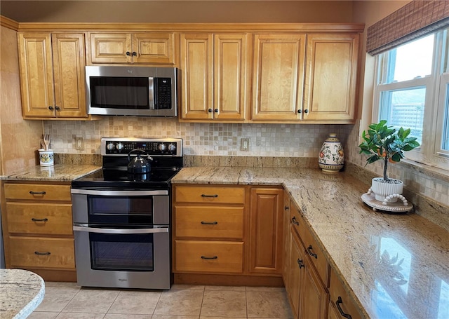 kitchen with stainless steel appliances, decorative backsplash, light stone counters, and light tile patterned floors