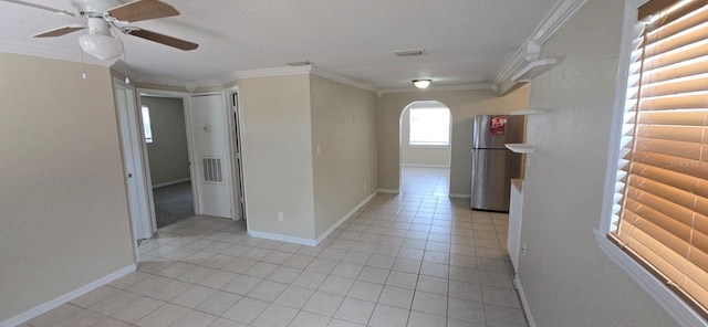 empty room featuring arched walkways, a ceiling fan, crown molding, light tile patterned floors, and baseboards