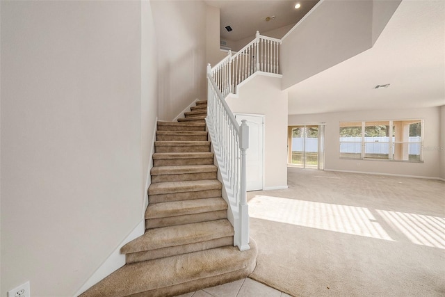 stairway featuring carpet flooring, a high ceiling, and baseboards